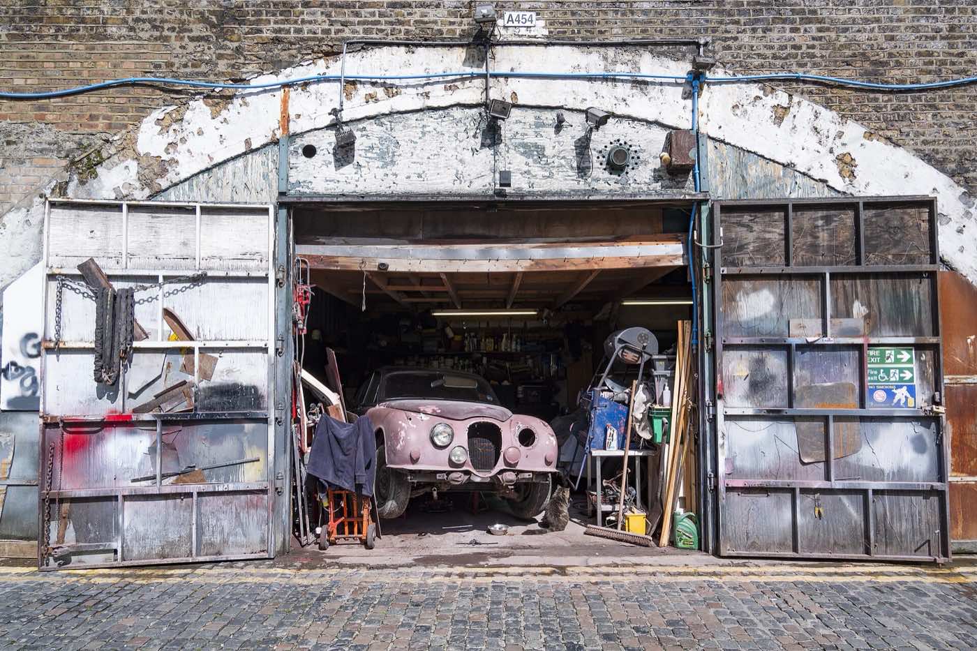 A brick arch on Andre Street with its metal doors open on a car repair workshop: an old car, tools and a trolley inside