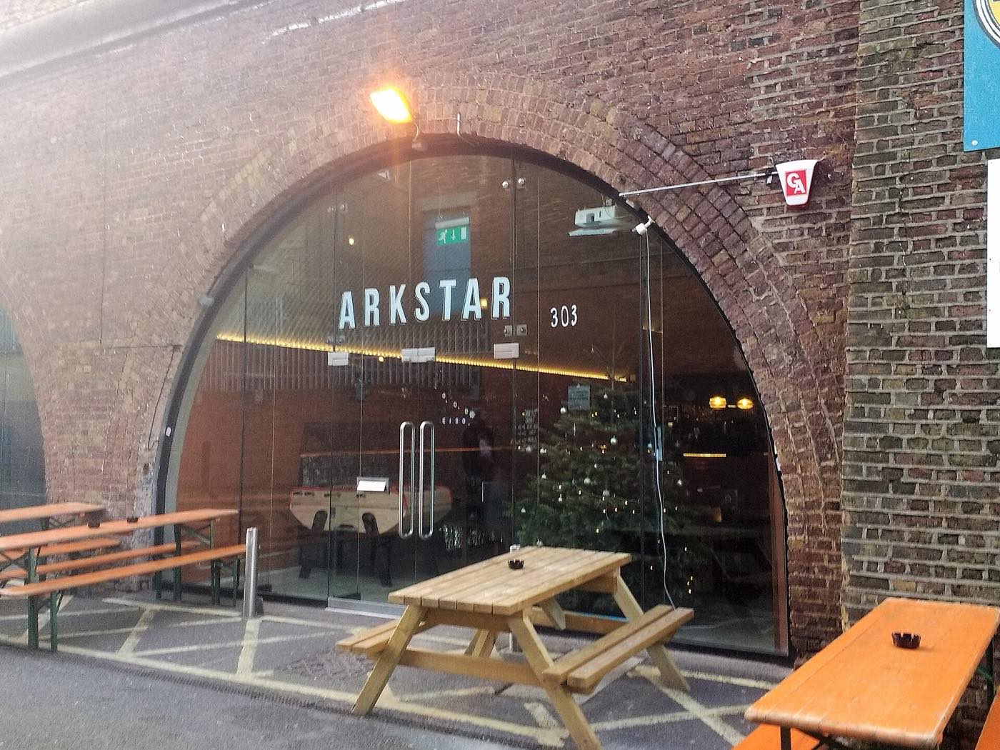 A brick railway arch with a fully glazed front fitted out as a bar, with wooden picnic benches outside